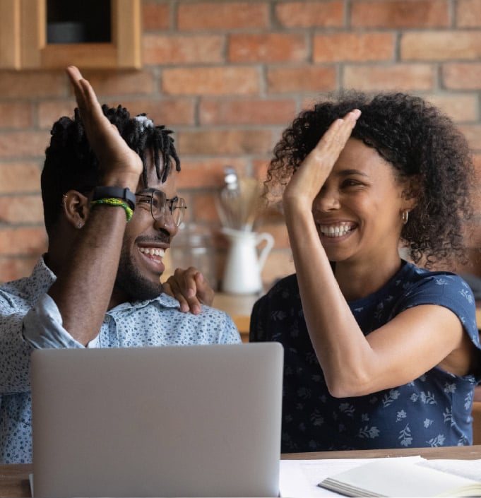 Couple sitting in front of a laptop high-fives.