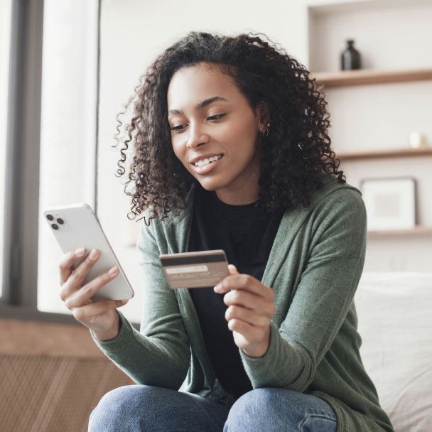 Woman makes a purchase from the comfort of her sofa using a credit card and her mobile phone.