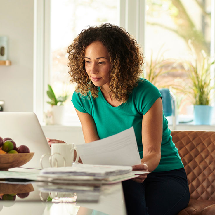 Woman looking through papers while sitting at her laptop