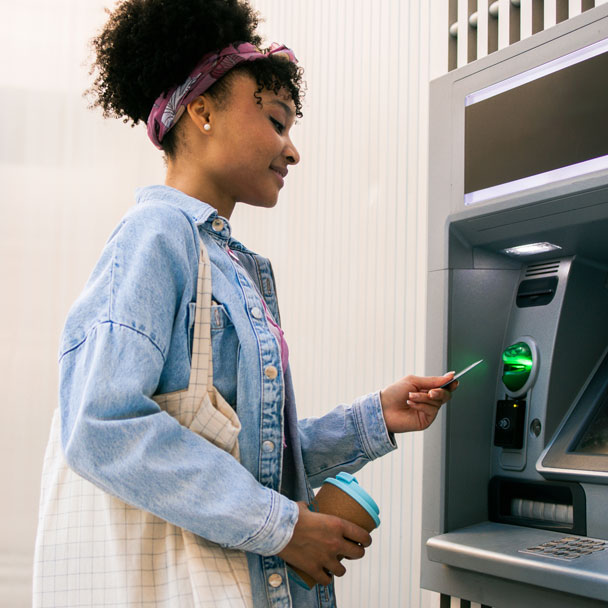 A young woman uses her debit card at an ATM.