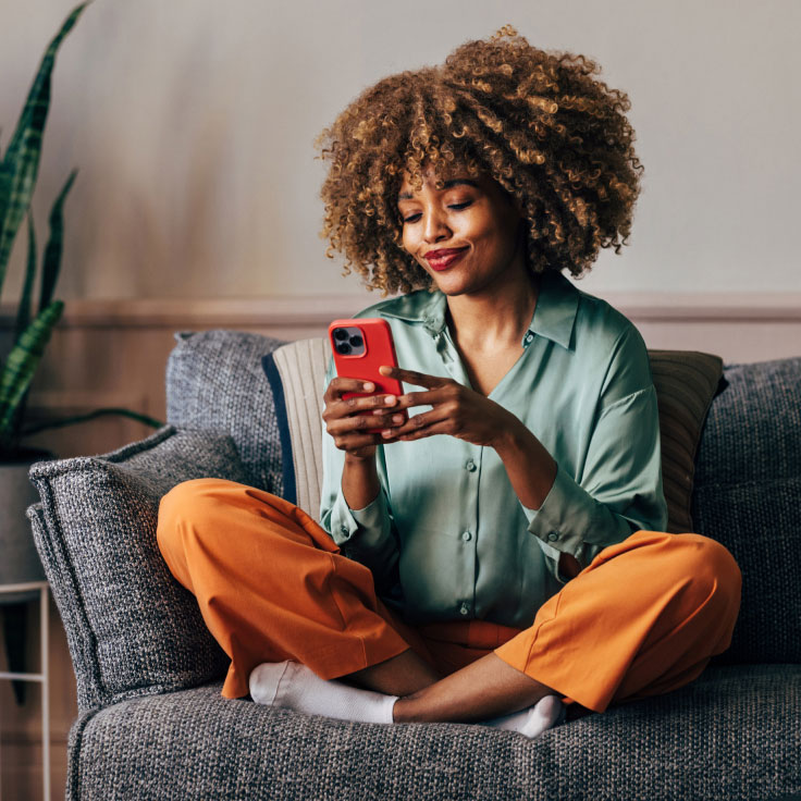 Young woman using her mobile phone to bank from the comfort of her sofa.