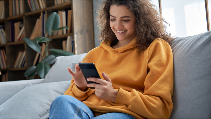 Woman sitting on her living room sofa and using a mobile device.