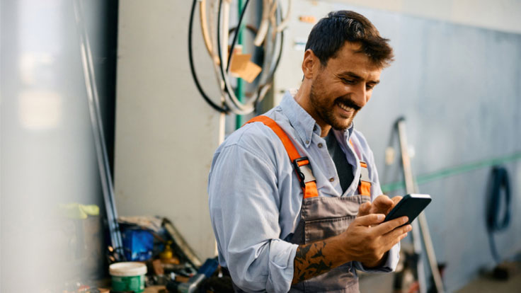 Man in coveralls looking up information on his phone.